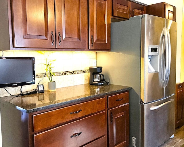 kitchen with dark stone counters, backsplash, and stainless steel fridge with ice dispenser