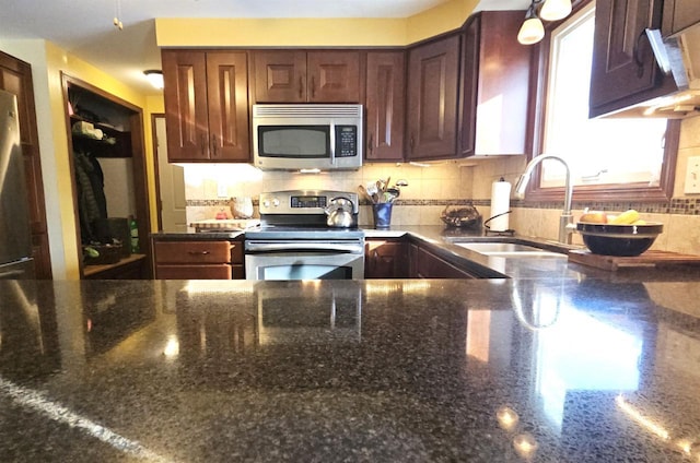 kitchen featuring backsplash, dark stone countertops, stainless steel appliances, and a sink