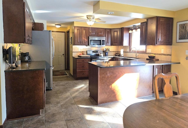 kitchen with stainless steel appliances, dark countertops, a sink, and a peninsula