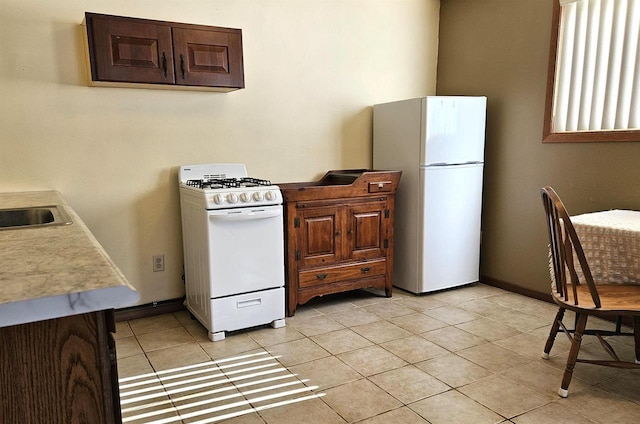 kitchen with light tile patterned floors, light countertops, a sink, white appliances, and baseboards