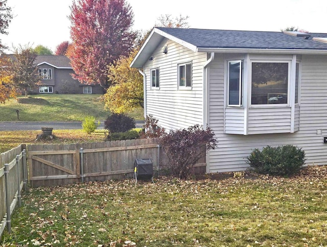 view of side of property with a shingled roof, fence, and a lawn