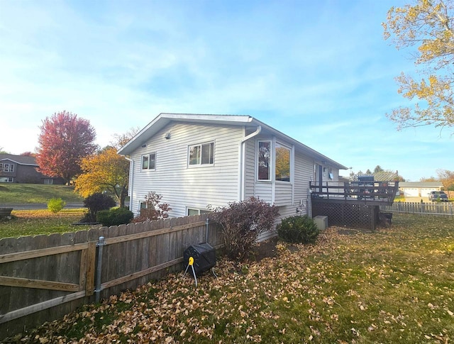 view of home's exterior featuring a lawn, a wooden deck, and fence