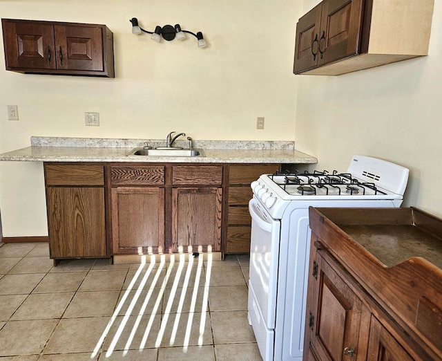 kitchen with light tile patterned floors, light countertops, white range with gas cooktop, a sink, and baseboards