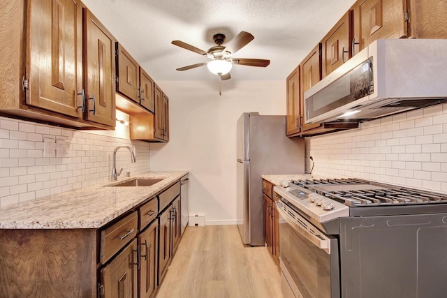 kitchen with ceiling fan, light wood-style flooring, stainless steel appliances, a sink, and brown cabinets