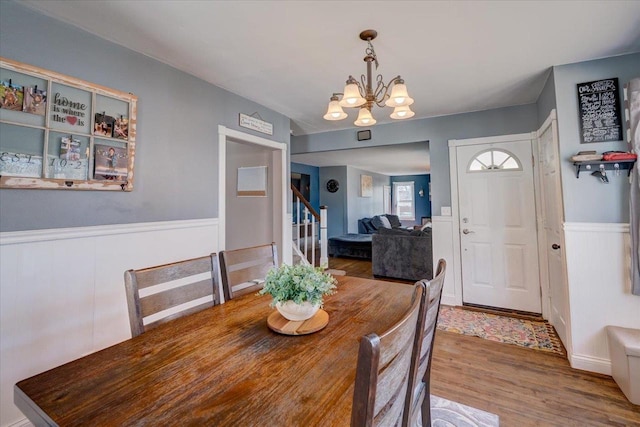 dining room with wainscoting, stairs, an inviting chandelier, and wood finished floors