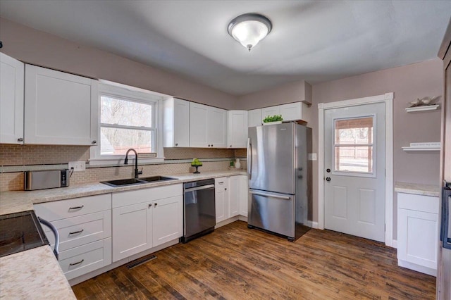 kitchen with backsplash, dark wood finished floors, appliances with stainless steel finishes, white cabinets, and a sink