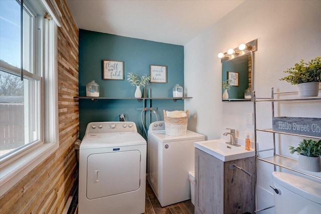 clothes washing area with a sink, laundry area, wood walls, and washer and clothes dryer