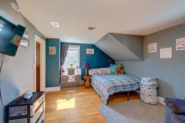 bedroom featuring visible vents, baseboards, light wood-style floors, and vaulted ceiling