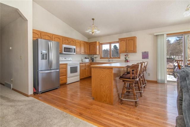 kitchen featuring a notable chandelier, visible vents, vaulted ceiling, white appliances, and a peninsula