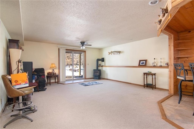 living area featuring baseboards, a ceiling fan, a wood stove, a textured ceiling, and carpet flooring