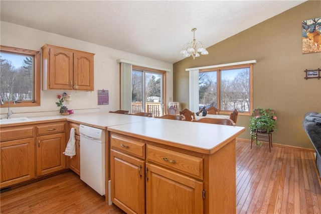 kitchen with a peninsula, light wood-style floors, vaulted ceiling, light countertops, and dishwasher