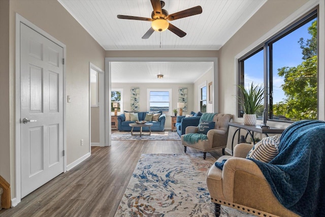 living area with ornamental molding, ceiling fan, baseboards, and wood finished floors