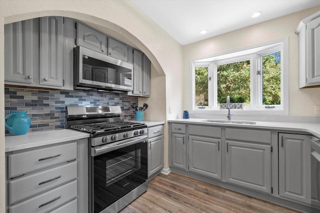 kitchen featuring stainless steel appliances, a sink, light wood-style floors, gray cabinets, and tasteful backsplash