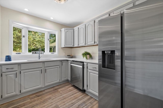 kitchen featuring light wood finished floors, appliances with stainless steel finishes, light countertops, gray cabinetry, and a sink