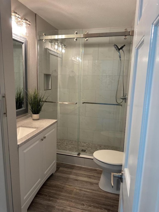 bathroom with a textured ceiling, toilet, wood finished floors, vanity, and a shower stall