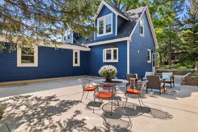 rear view of property featuring a shingled roof, a patio area, and an outdoor hangout area