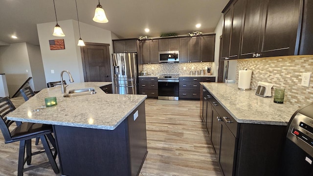 kitchen featuring a breakfast bar area, appliances with stainless steel finishes, vaulted ceiling, a sink, and light wood-type flooring