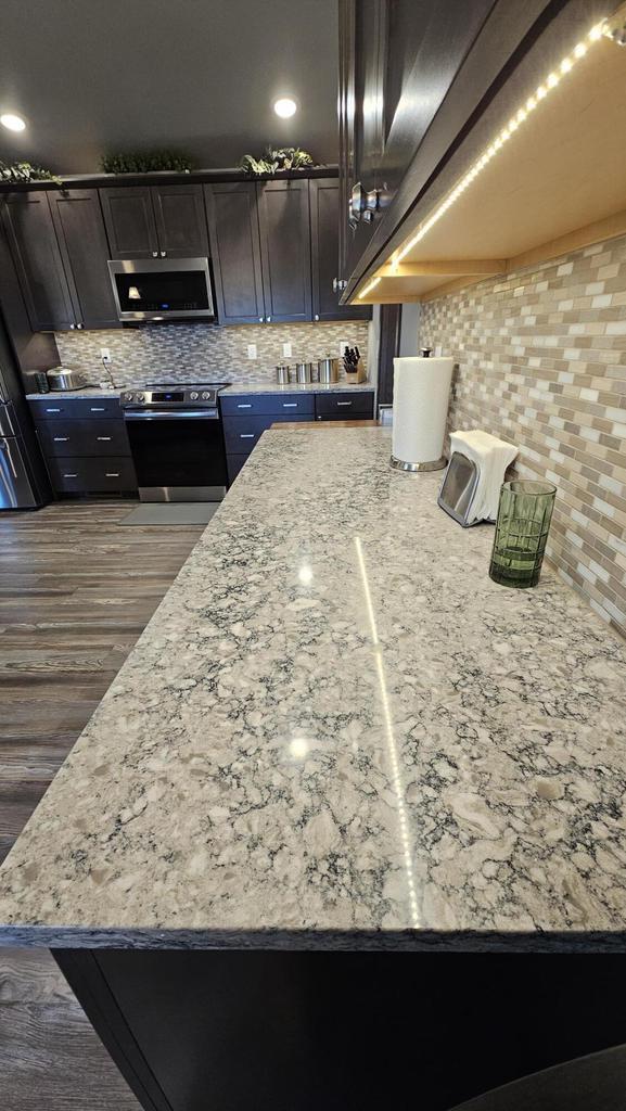 kitchen with dark wood-style flooring, tasteful backsplash, appliances with stainless steel finishes, dark brown cabinetry, and light stone countertops