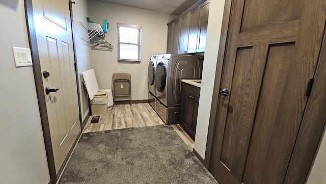 laundry room featuring light carpet, baseboards, light wood-style floors, cabinet space, and washer and clothes dryer