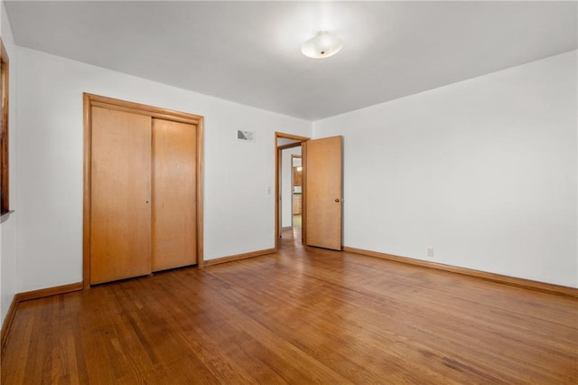 unfurnished bedroom featuring a closet, wood finished floors, visible vents, and baseboards