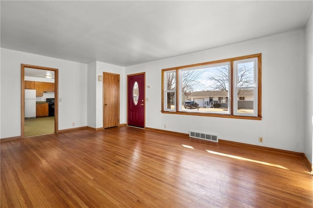 unfurnished living room with wood-type flooring, visible vents, and baseboards