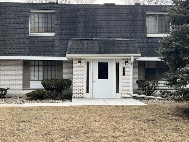 view of front of home with a front yard, mansard roof, brick siding, and roof with shingles