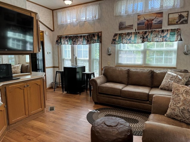 living area with visible vents, ornamental molding, and light wood-style flooring