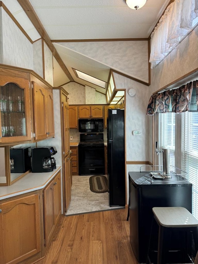 kitchen featuring brown cabinets, light countertops, light wood-style flooring, lofted ceiling with beams, and black appliances