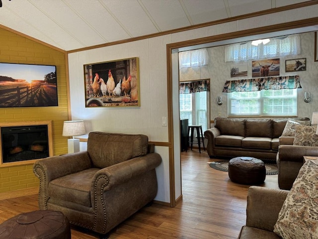 living area with lofted ceiling, crown molding, a fireplace, and wood finished floors