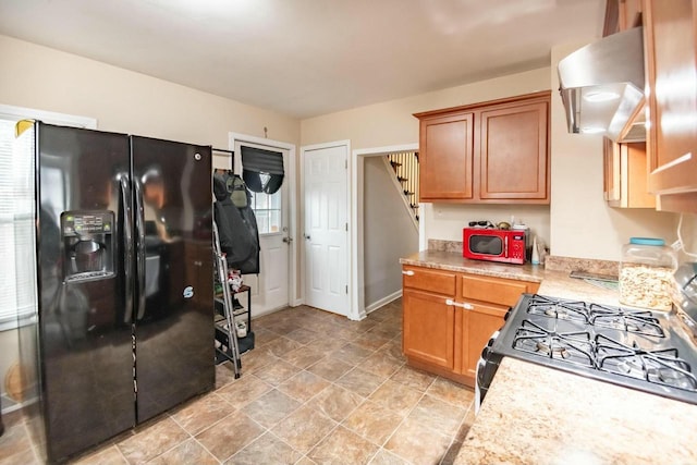 kitchen with black fridge with ice dispenser, wall chimney exhaust hood, brown cabinets, gas range oven, and light countertops