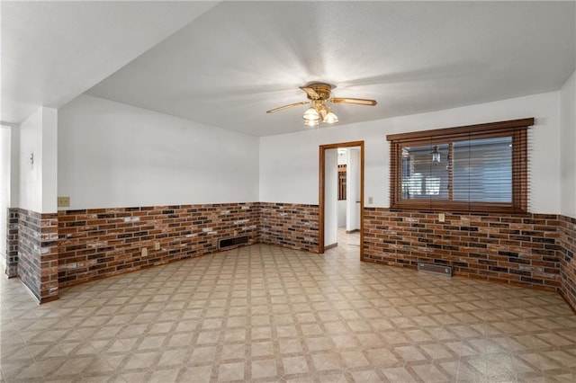 spare room featuring a wainscoted wall, brick wall, light floors, and a ceiling fan