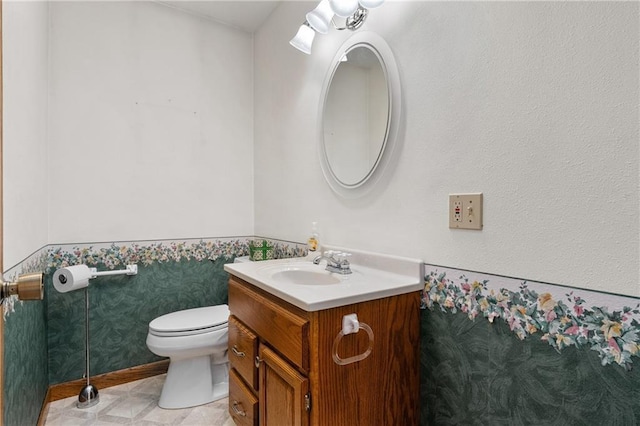 half bath with wainscoting, vanity, and toilet