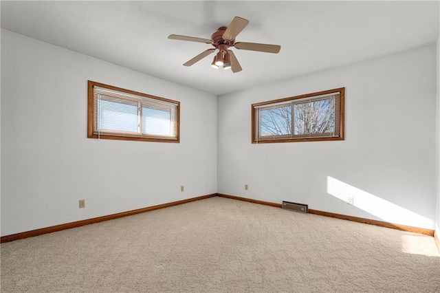 carpeted spare room with baseboards, visible vents, and a ceiling fan