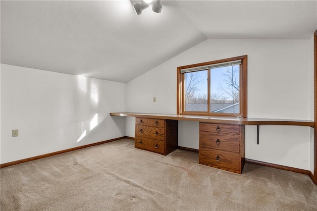 unfurnished office featuring carpet flooring, vaulted ceiling, built in desk, and baseboards