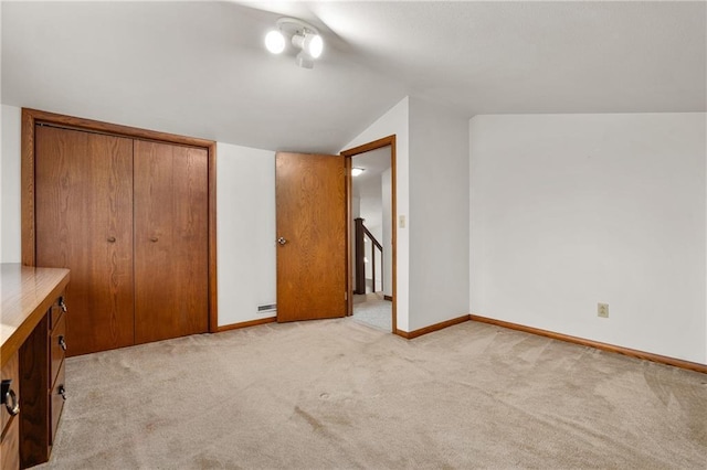 unfurnished bedroom featuring lofted ceiling, a closet, light carpet, and baseboards