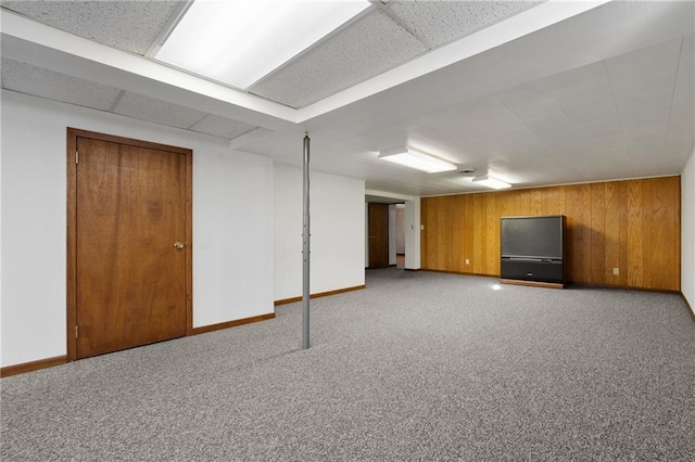 basement with a paneled ceiling, wood walls, carpet, and baseboards