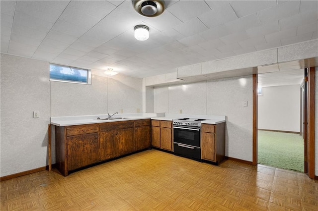 kitchen with baseboards, brown cabinetry, light countertops, a sink, and range with electric stovetop