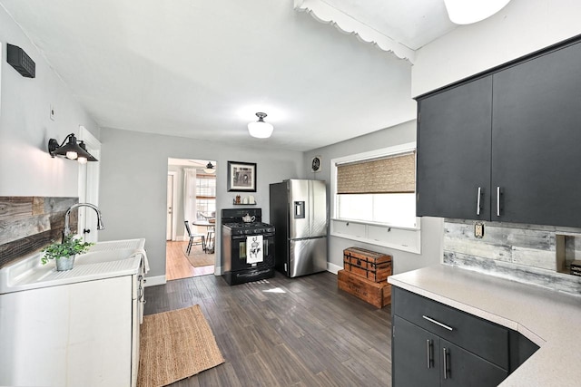 kitchen featuring black range with gas cooktop, dark cabinets, light countertops, stainless steel fridge with ice dispenser, and dark wood-style floors