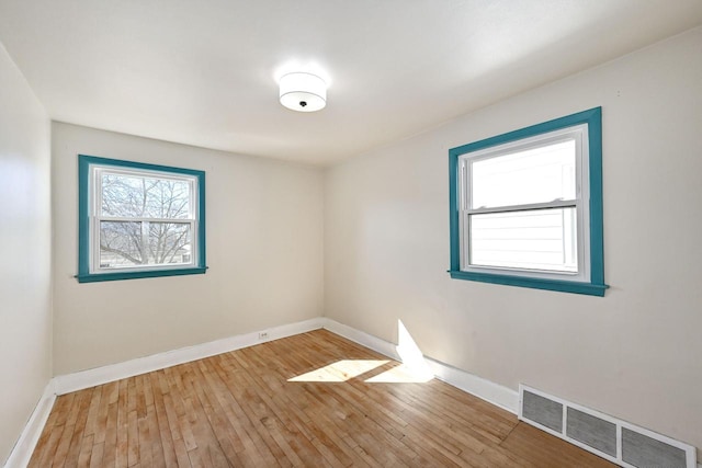 spare room with hardwood / wood-style floors, visible vents, and baseboards