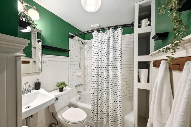 bathroom featuring toilet, shower / bathtub combination with curtain, a sink, and wainscoting