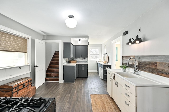 kitchen with a sink, light countertops, gray cabinets, decorative backsplash, and dark wood-style floors