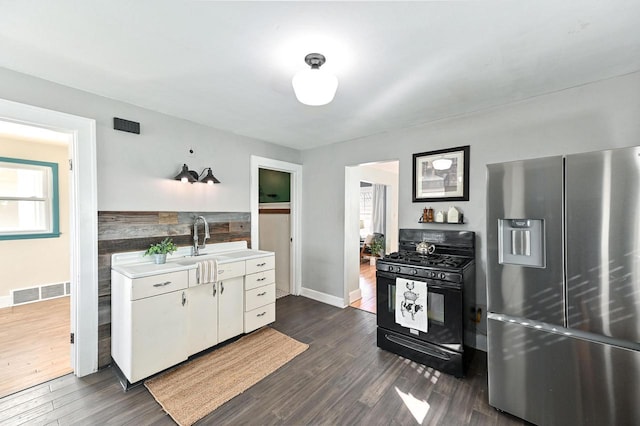 kitchen featuring stainless steel fridge, visible vents, white cabinets, black gas stove, and a sink