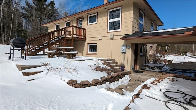 snow covered rear of property featuring stairs and a chimney