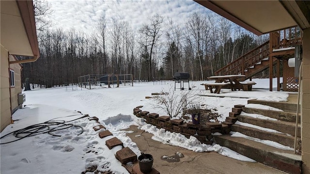 yard layered in snow with stairs and a wooded view