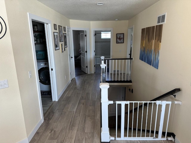 hall featuring visible vents, a textured ceiling, wood finished floors, washer / dryer, and baseboards