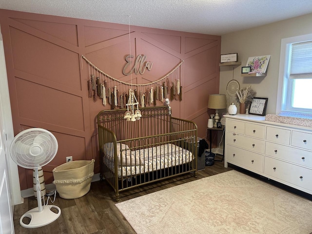 bedroom with a crib, a textured ceiling, and wood finished floors