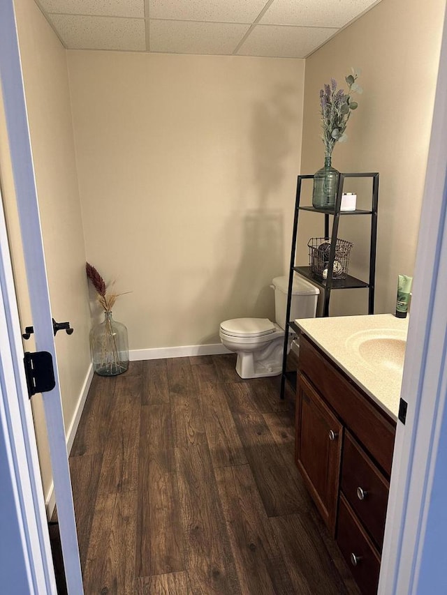 bathroom with baseboards, a drop ceiling, toilet, wood finished floors, and vanity