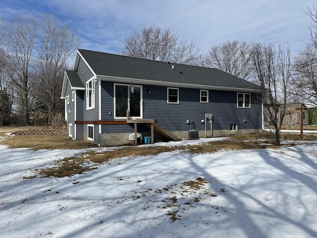 snow covered house featuring a shingled roof, central air condition unit, and stairs