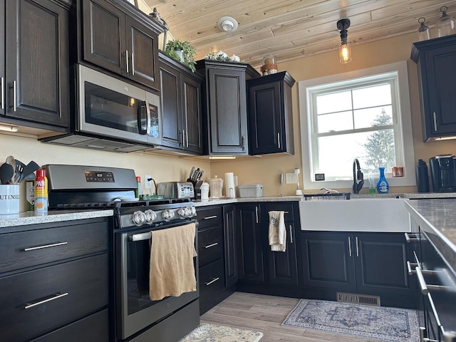 kitchen with visible vents, appliances with stainless steel finishes, a sink, light wood-type flooring, and wooden ceiling