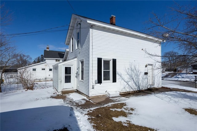 snow covered property with entry steps and a chimney